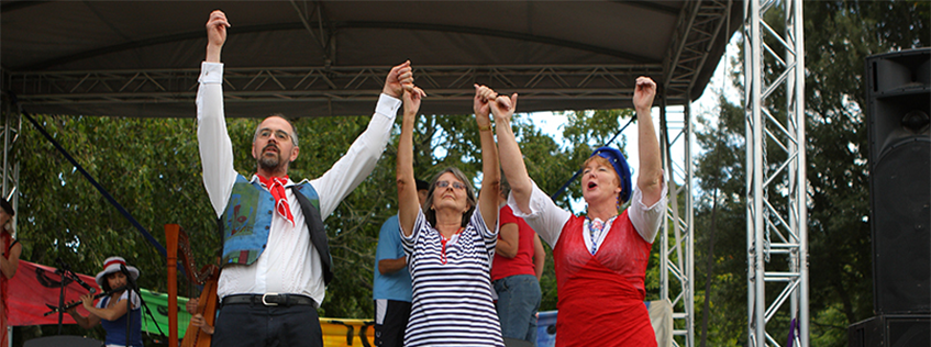 Image of three people dancing, their hands are entwined with their arms in the air.